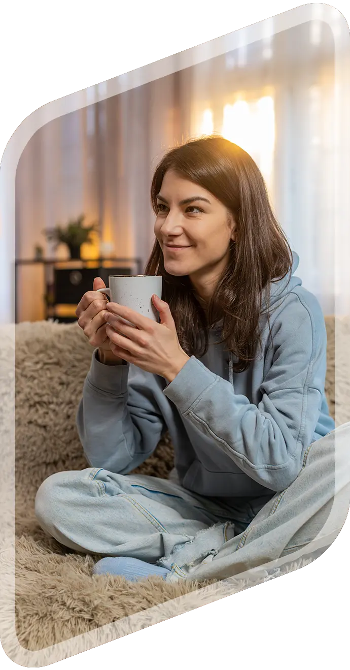 Woman in hoodie holding a mug on a sofa
