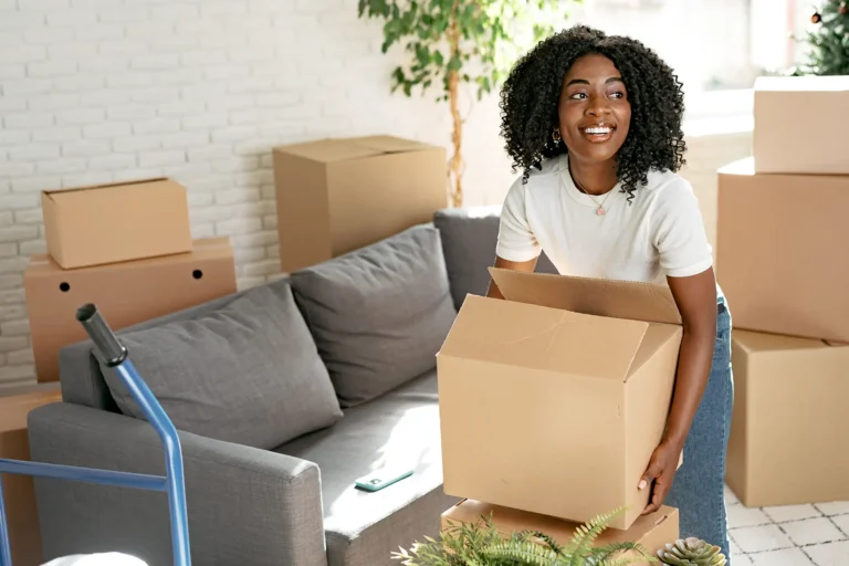Woman holding moving box in living room with packed boxes