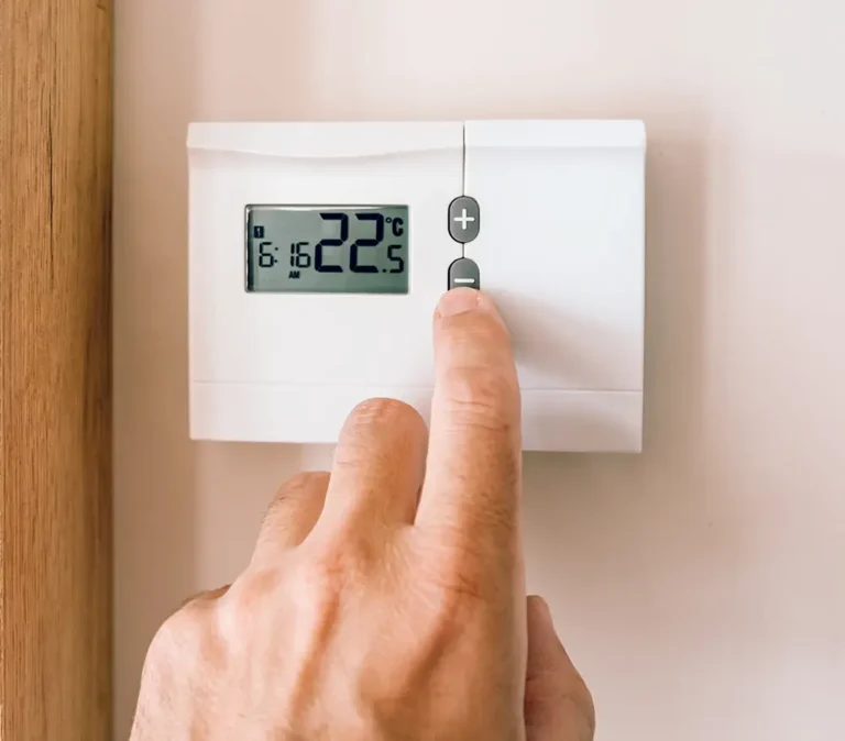 Hand lowering a wall thermostat set to 22.5°C