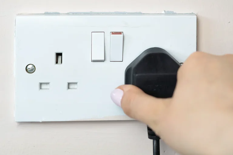 Hand plugging black plug into UK wall socket