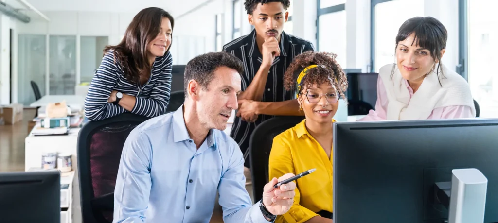 Diverse colleagues collaborating around a computer in a bright office