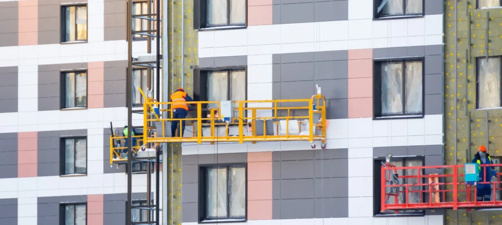 Construction workers installing cladding on apartment building from lifting platforms