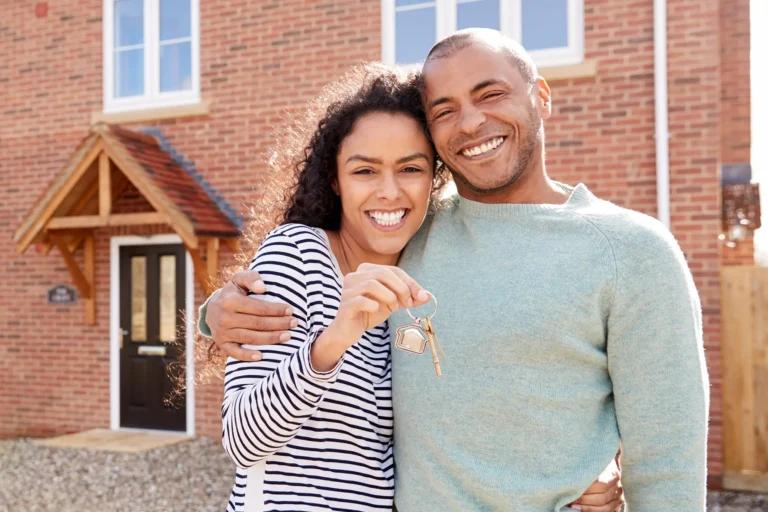 Smiling couple holding house keys outside their new home