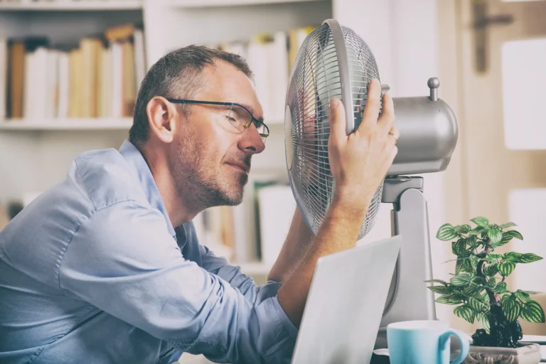 Man cooling himself with desk fan at office