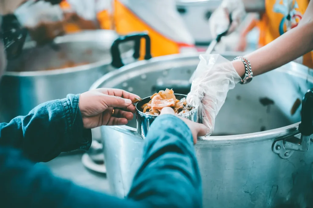 Gloved worker serves food from a large cooking pot