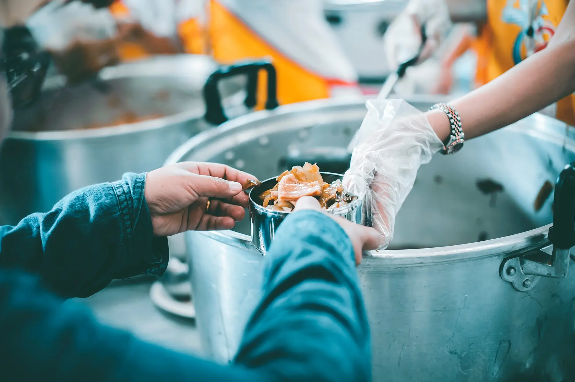 Gloved worker serves food from a large cooking pot