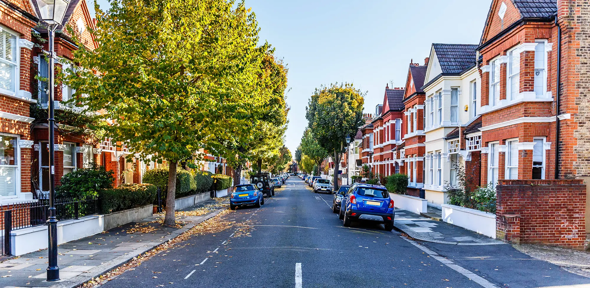 Tree-lined residential street with red-brick houses and parked cars