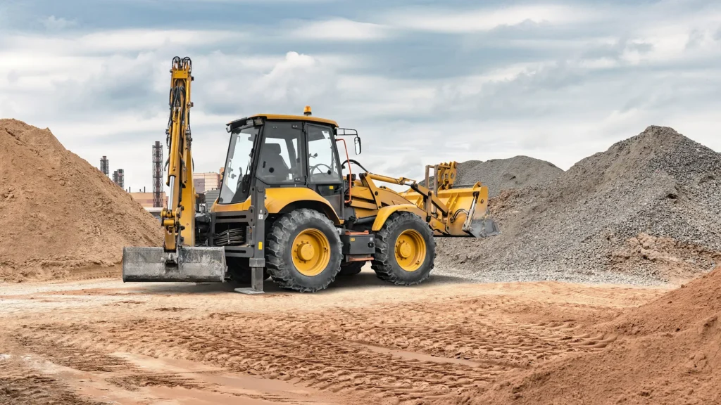 Yellow backhoe loader between sand and gravel piles