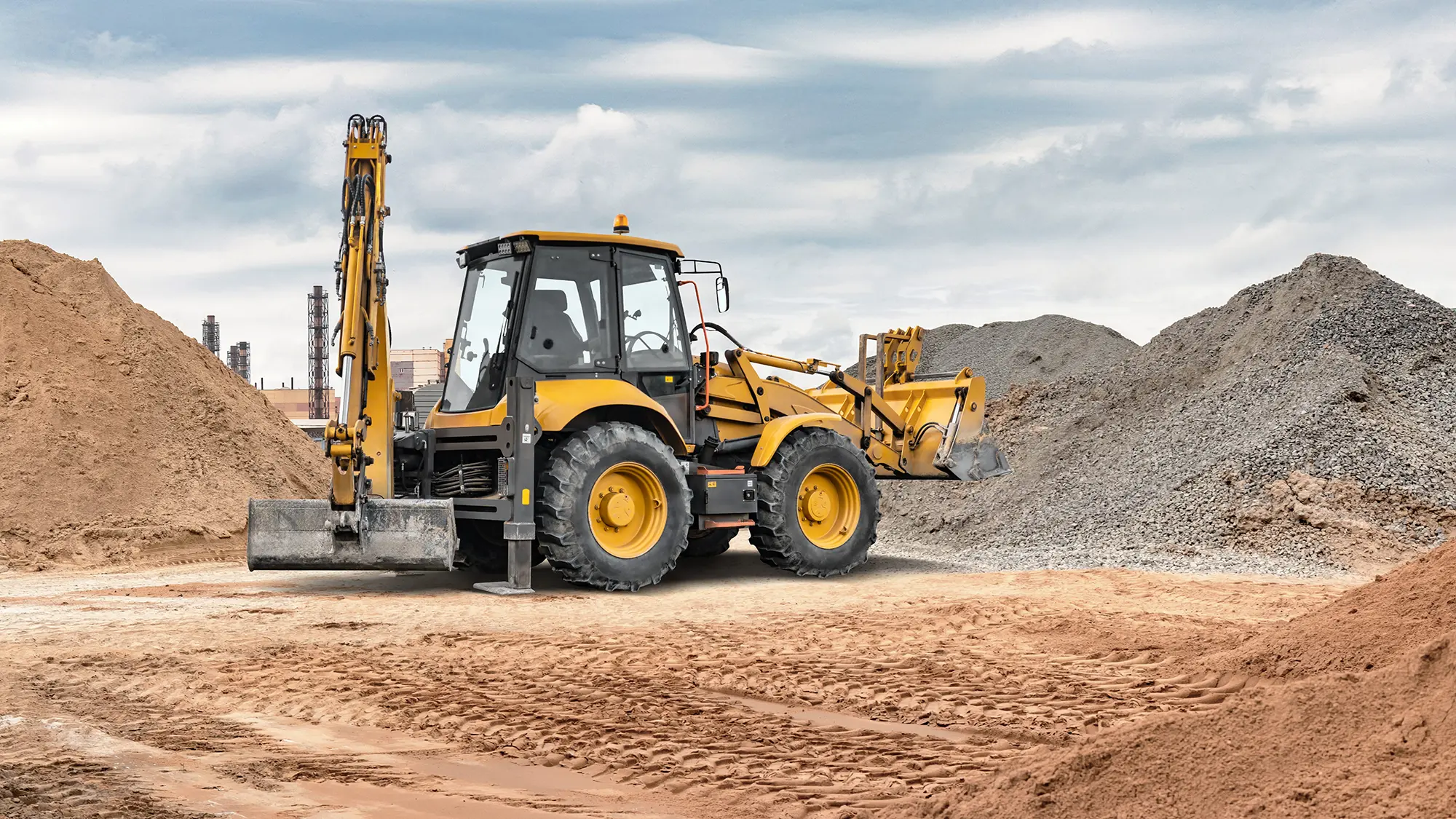 Yellow backhoe loader between sand and gravel piles